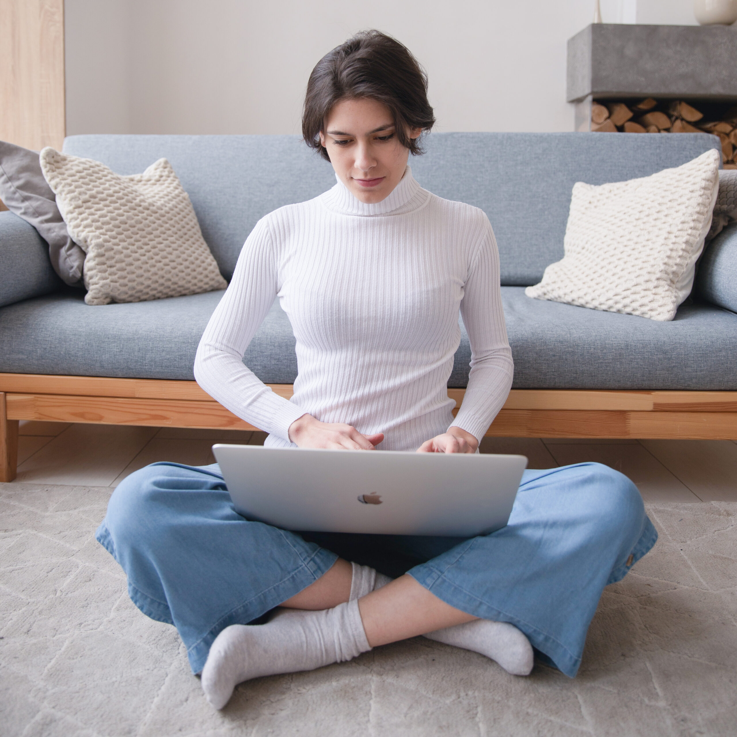 Woman sitting cross-legged on floor reading on laptop
