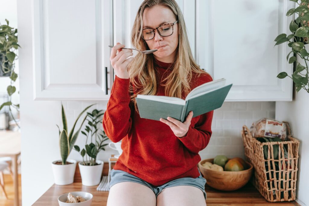Woman sitting on kitchen counter reading a book and eating